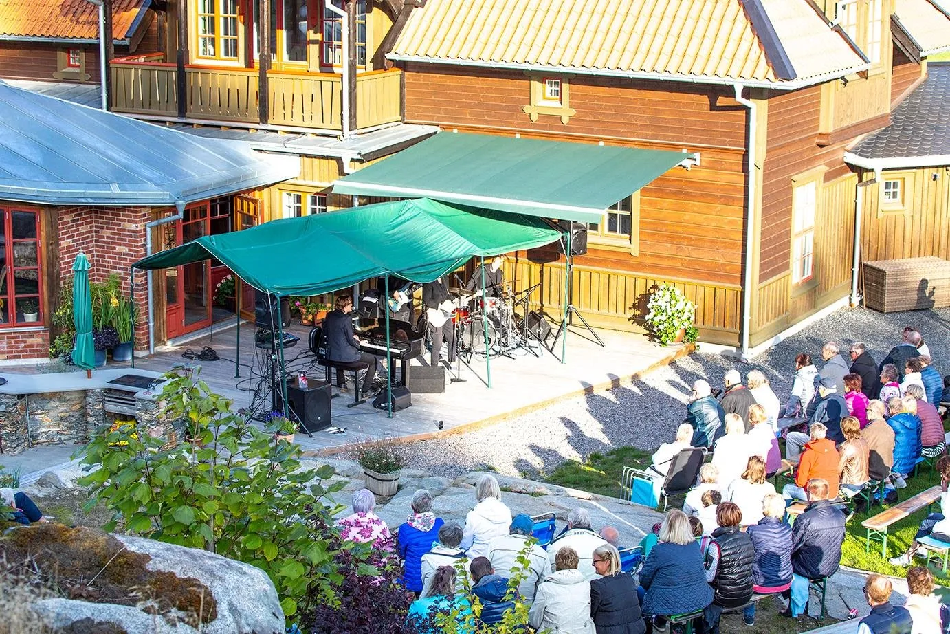 Bandet spelar under gröna parasoller vid huset medan publiken sitter på klipporna