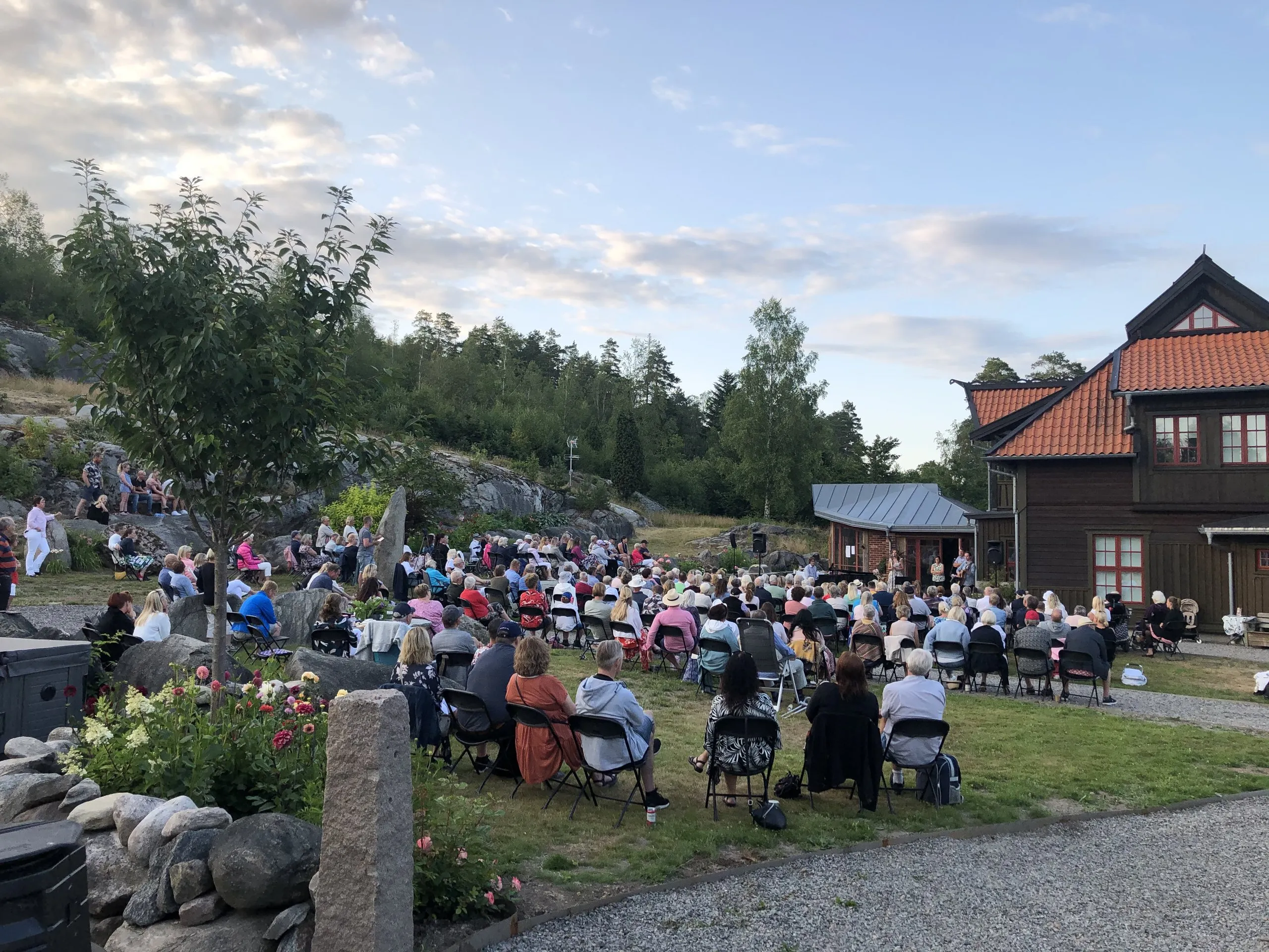 Publiken sitter på gräsmattan framför huset under konserten